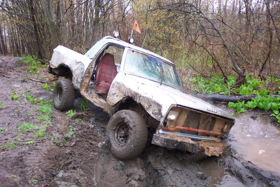 White pickup truck stuck in mud, driver's door open, red interior visible, orange flag on roof