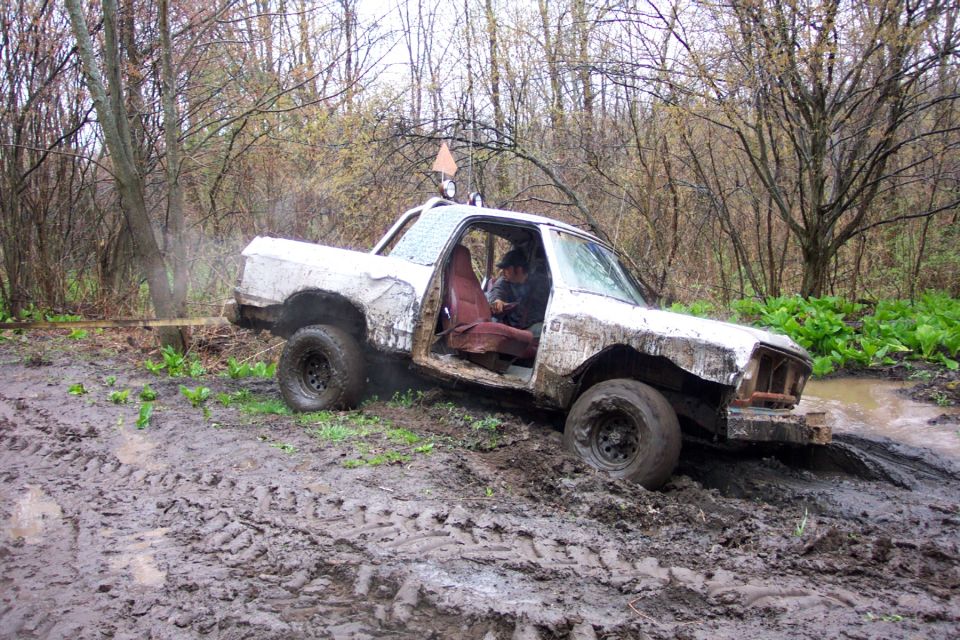 White off-road vehicle with open door stuck in mud, trees and foliage in background
