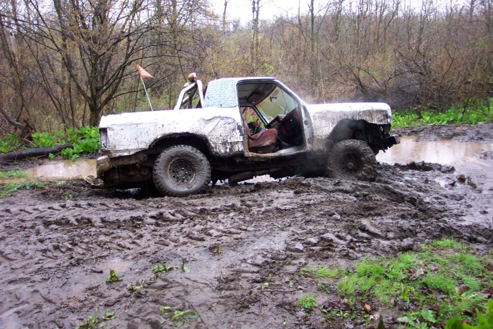 White pickup truck with doors removed stuck in deep mud, trees and brush in background