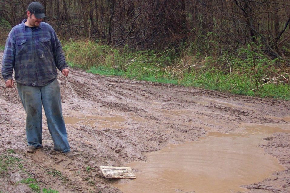 Man pulling a keyboard through a muddy road with tire tracks