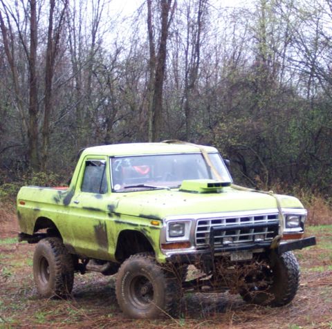 1978 Ford Bronco - Modified pickup truck with a hood scoop and off-road tires sits in a wooded area.