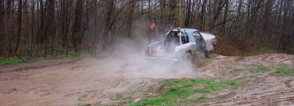 Off-road truck driving through mud and dust on a wooded trail