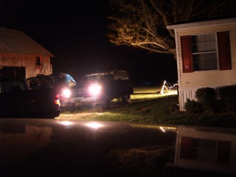 1988 Ford Bronco - A 1988 Ford Bronco is seen at night with its headlights illuminated, parked near a barn and a mobile home.
