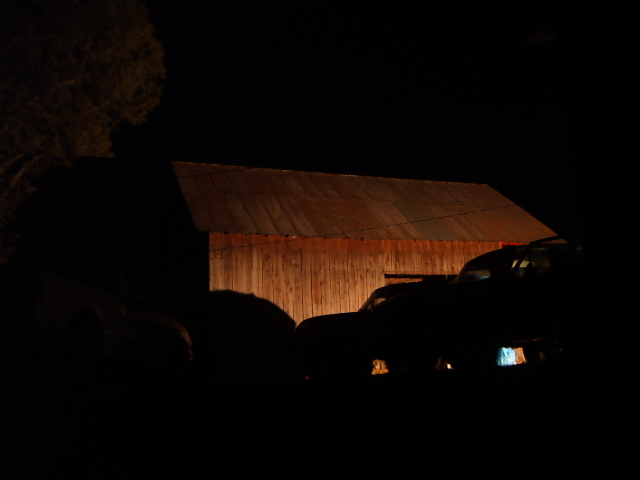 two vehicles silhouetted in front of a lit barn at night