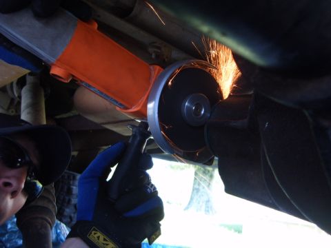 1988 Ford Bronco - Cutting a vehicle's exhaust pipe with an angle grinder, sparks flying.