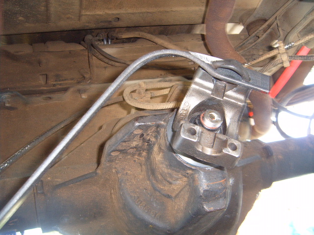 Driveshaft connected to a dirty differential housing with brake lines and exhaust pipe visible