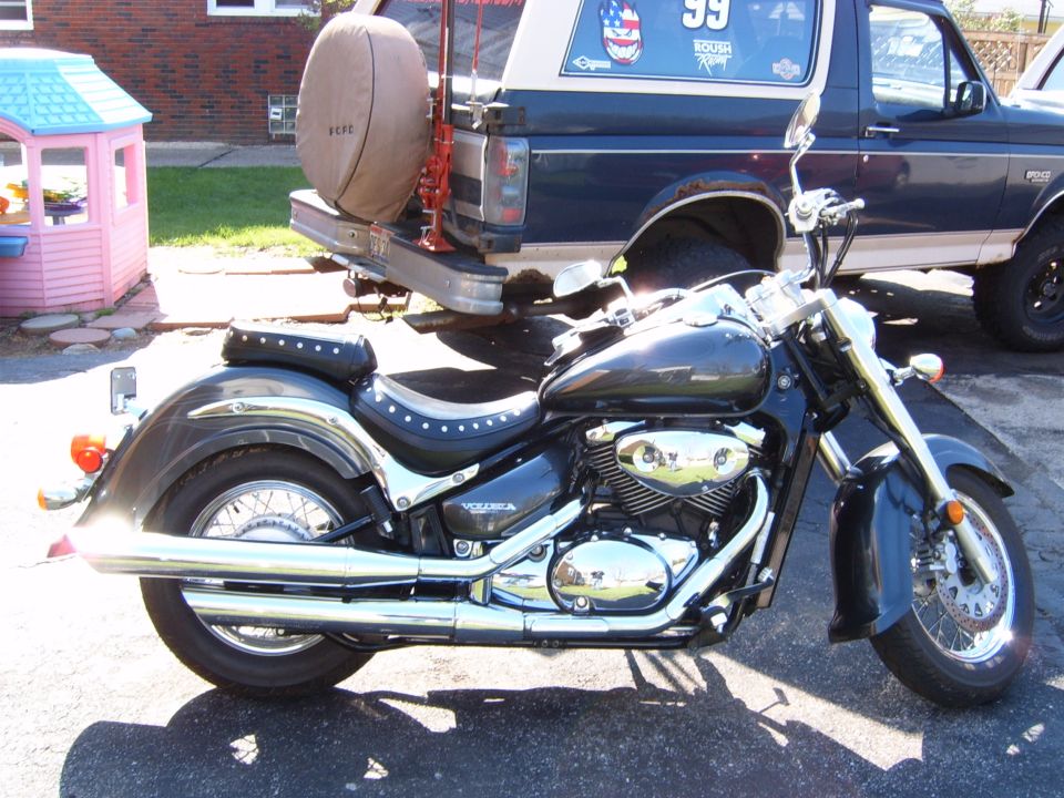 Dark gray motorcycle parked in front of a blue Ford Bronco with a spare tire on the back