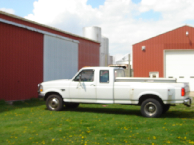 White pickup truck parked on grass in front of red barns