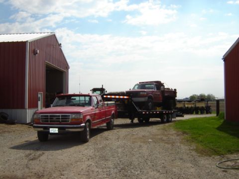 1992 Ford Bronco - A red 1992 Ford F-250 pickup truck tows a red Ford F-350 pickup truck on a trailer near a red barn.