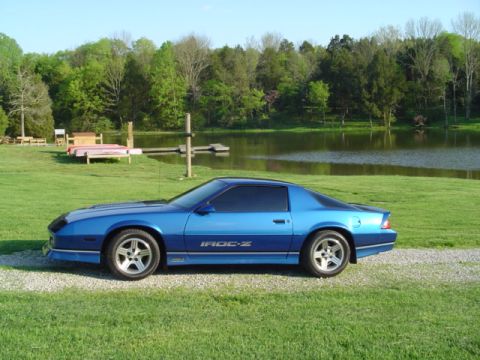2001 Ford Crown Victoria - A blue IROC-Z Camaro is parked on a gravel driveway next to a grassy lawn and a lake.