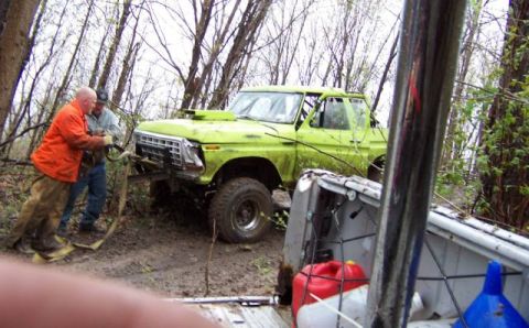 1978 Ford Bronco - Two men winch a lime green, off-road modified truck out of a muddy, wooded area.