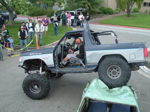 1989 Ford Bronco - A heavily modified 1989 Ford Bronco demonstrates its off-road capability by driving over a crushed vehicle.