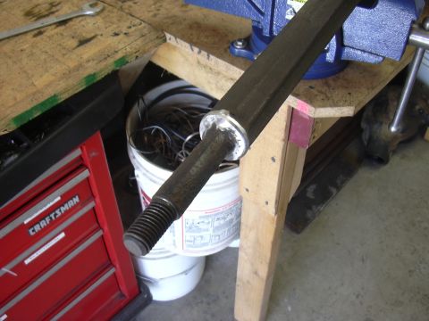 1991 Ford Bronco - A long steel steering or track-bar shaft clamped in a blue bench vise on a plywood workbench, its threaded end and freshly ground/welded sh…