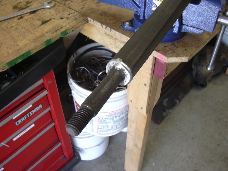 Threaded steel steering shaft clamped in blue bench vise in garage workshop