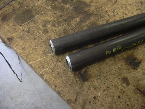 1991 Ford Bronco - Two cut metal tubes lie on a worn workbench, one marked with a part number.