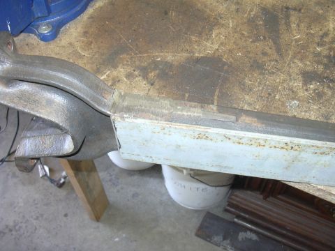 1991 Ford Bronco - A metal suspension component is secured in a vise on a cluttered workbench.