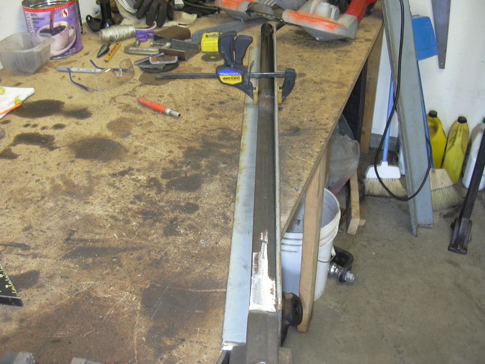 Metal part clamped to a workbench with tools and supplies in the background