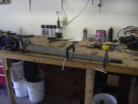 1991 Ford Bronco - A metal component is secured to a workbench with clamps, surrounded by various tools and supplies.