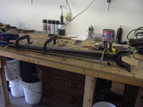 1991 Ford Bronco - A metal part is secured with clamps on a workbench, surrounded by workshop supplies.