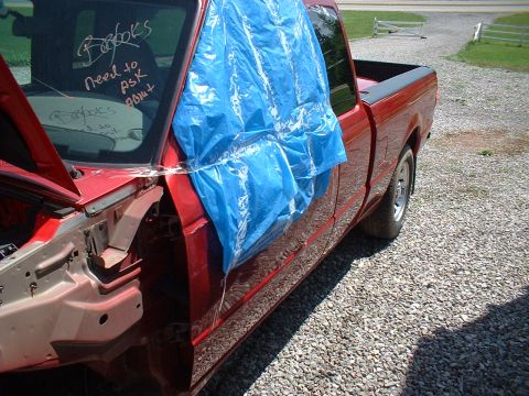 1999 Ford Ranger - A red 1999 Ford Ranger pickup truck sits on a gravel surface, with the driver's side door covered by a blue tarp and notes scrawled on the…