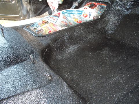 1978 Ford Bronco - The interior floor of a vehicle is covered in black textured material, with newspaper visible in a compartment.