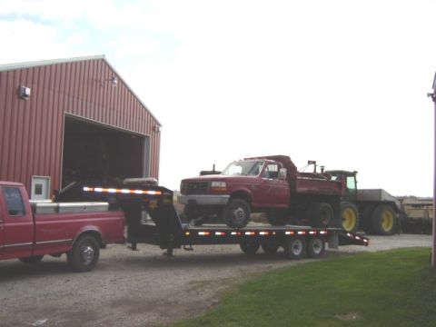 1992 Ford Bronco - A red dump truck and tractor are transported on a trailer towed by a pickup truck.