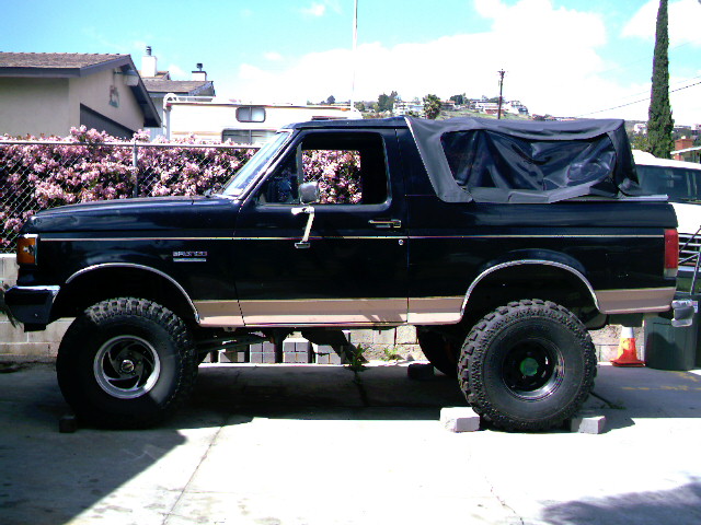 Black Ford Bronco with tan stripe, lifted, black soft top, side view