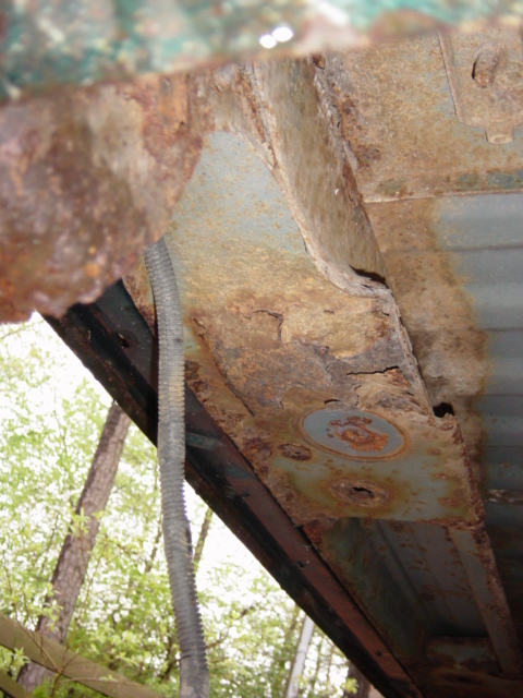 1991 Ford Bronco - Close-up of heavily rusted vehicle frame components and hanging conduit.