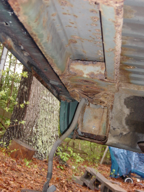1991 Ford Bronco - Close-up view of a heavily rusted vehicle frame section, showing structural degradation and a dangling wiring harness.