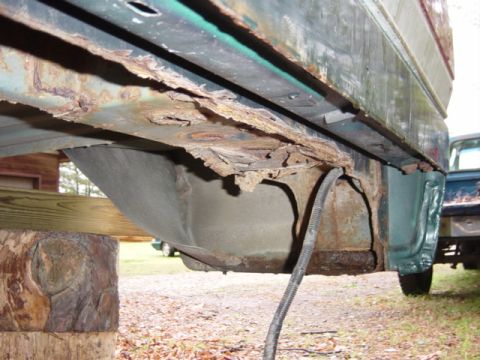 1991 Ford Bronco - Extensive rust damage is visible on the vehicle's frame and undercarriage, with a black hose hanging down. Another vehicle is partially see…