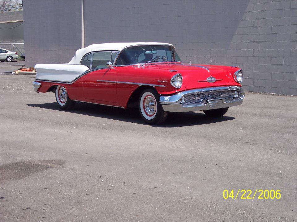 Red 1957 Oldsmobile convertible with white top, front three-quarter view