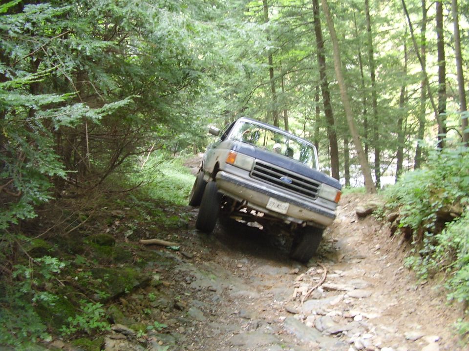 Blue and grey Ford F-Series truck on a rocky, wooded trail