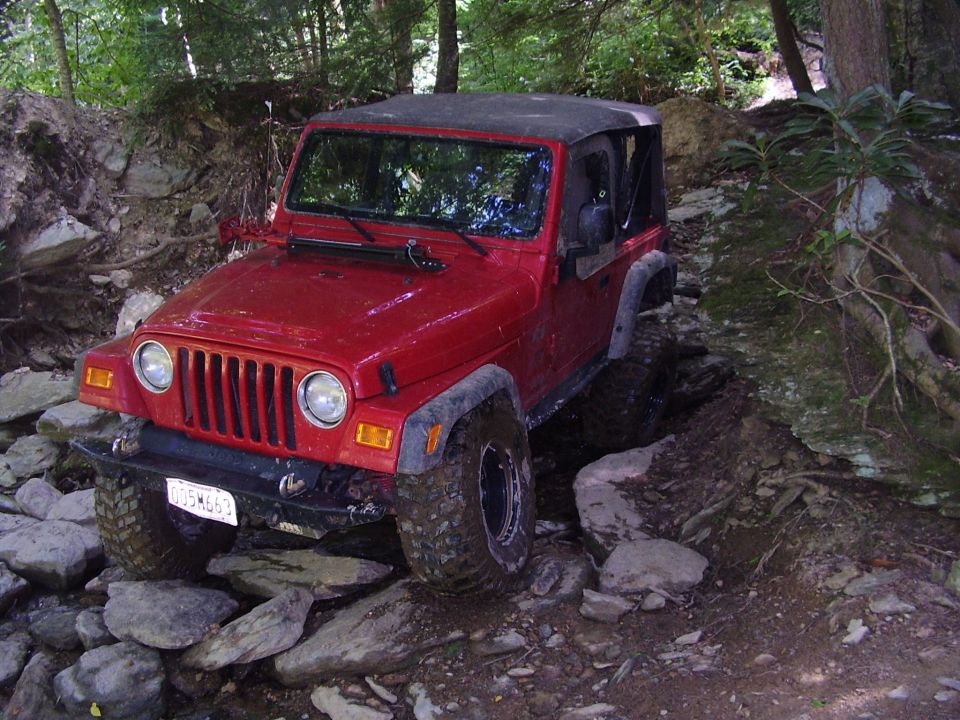 Red 2003 Jeep Wrangler navigating a rocky trail