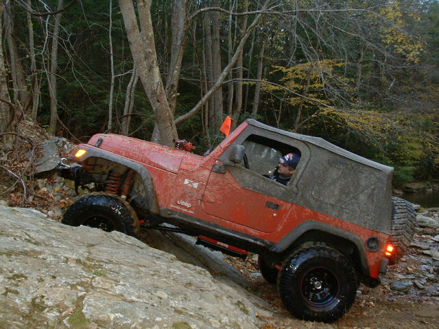 Red 2003 Jeep Wrangler climbing a rocky incline with a soft top