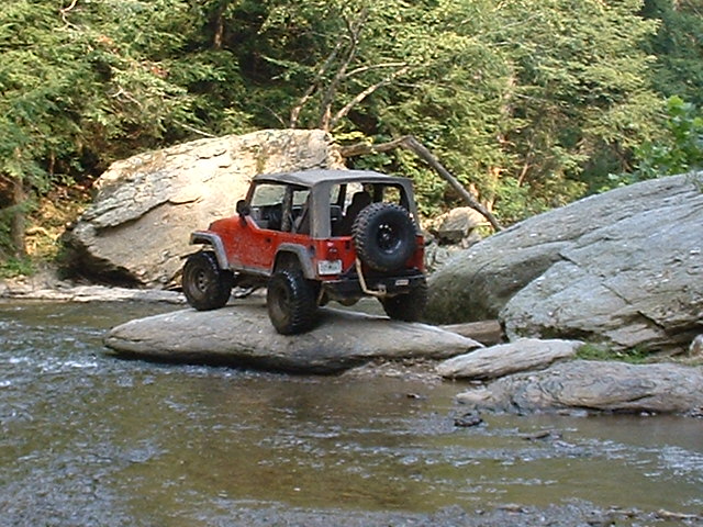 Red 2003 Jeep Wrangler on rocks in a stream