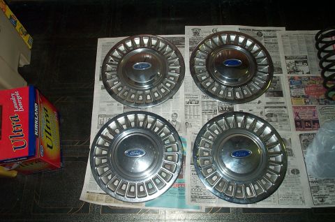 1991 Ford Crown Victoria LTD - A set of four Ford hubcaps are displayed on top of old newspapers.