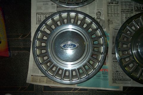 1991 Ford Crown Victoria LTD - A single Ford hubcap is shown, resting on newspaper with advertisements.