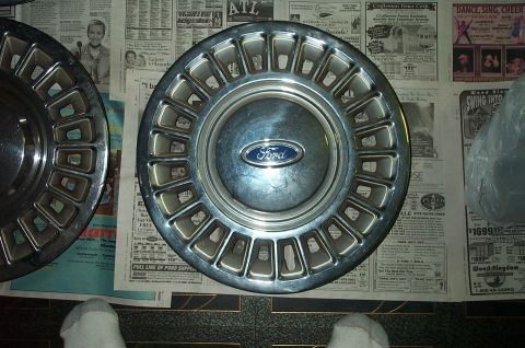 1991 Ford Crown Victoria LTD - A single Ford hubcap is shown, centered on a newspaper background. Another hubcap is partially visible to the left.