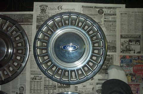 1991 Ford Crown Victoria LTD - A single Ford hubcap is shown against a backdrop of old newspapers.