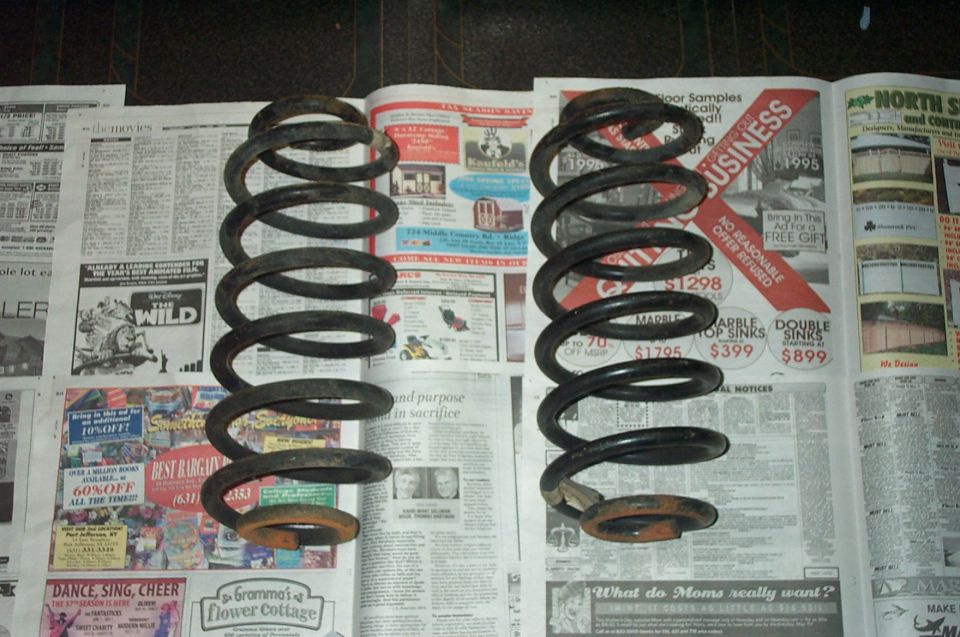 Pair of used coil springs standing on newspaper, black paint with rusty ends