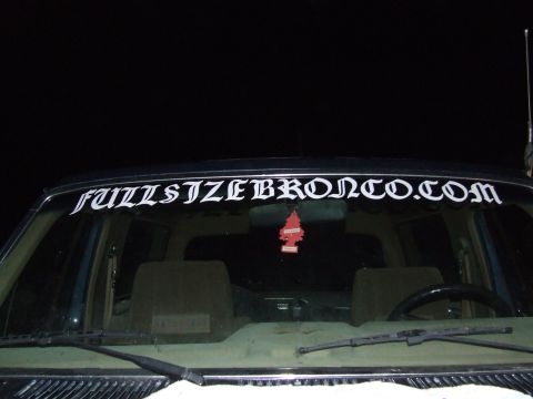 1986 Ford Bronco - Interior view of a vehicle with a custom windshield banner and an air freshener hanging from the rearview mirror.