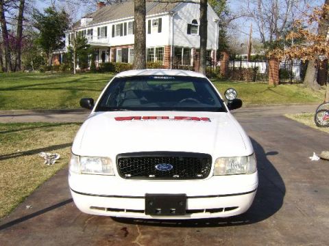 1999 Ford Crown Victoria - A white Ford Crown Victoria is parked in front of a large white house.