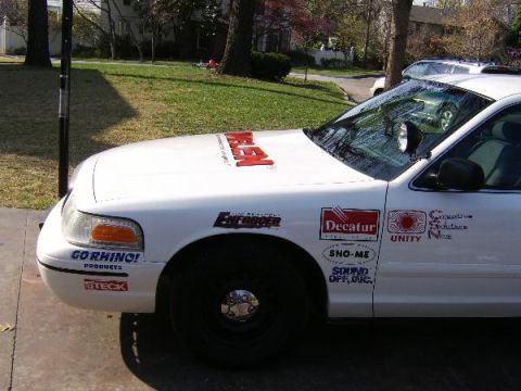 1999 Ford Crown Victoria - White 1999 Ford Crown Victoria police car with various decals on its side and hood.
