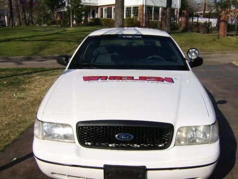 1999 Ford Crown Victoria - This white sedan features a Whelen logo on its hood, indicating it may be equipped with emergency lighting or related equipment.