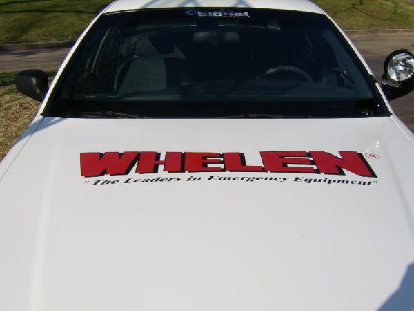 White car hood with red "WHELEN" lettering and "The Leaders in Emergency Equipment" text below