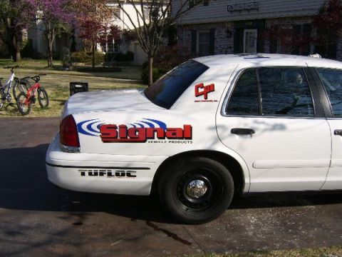 1999 Ford Crown Victoria - A white sedan is seen from the rear quarter with prominent 'Signal Vehicle Products' and 'Tufloc' decals on its body.