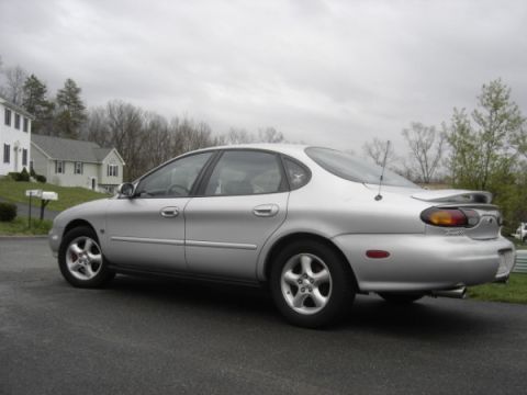 1999 Ford Taurus - The rear 3/4 view of a silver 1999 Ford Taurus sedan shows its distinctive taillights and spoiler.