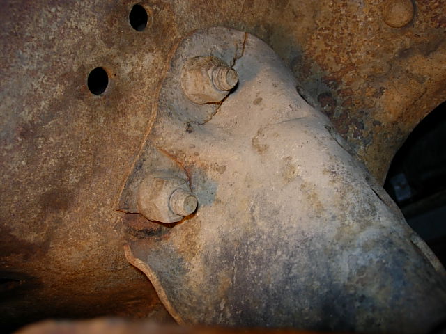 Close-up of a cracked metal suspension bracket held by two large bolts