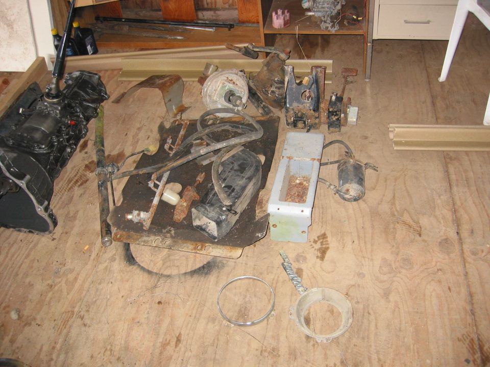 Engine block and various rusty metal vehicle parts scattered on a wooden floor