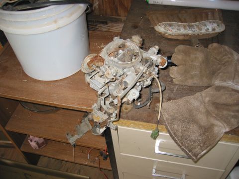 1991 Ford Explorer - A heavily corroded carburetor sits on a workbench next to a white bucket and protective gloves.